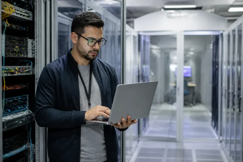 A cybersecurity engineer inspecting network equipment in a server room during a meeting.