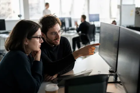 Cybersecurity professionals reviewing vulnerability data on multiple computer screens in a modern office setting.