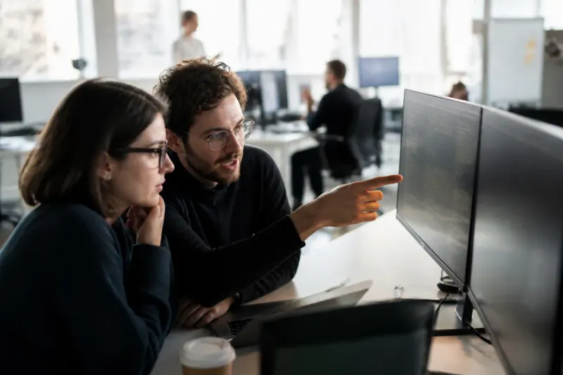 Cybersecurity professionals reviewing vulnerability data on multiple computer screens in a modern office setting.