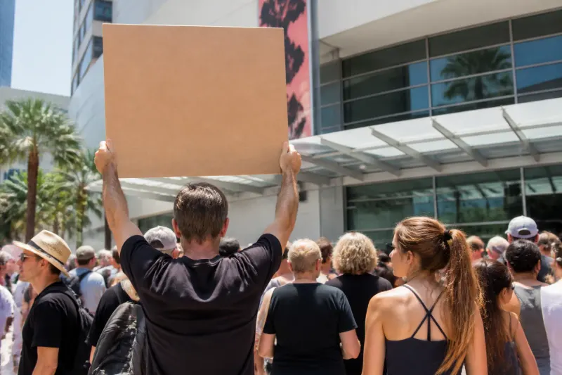 A protestor holds a sign criticizing the use of video game mechanics in political themes.