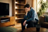 A gamer sitting in a living room with an empty game shelf, looking at a PlayStation console.