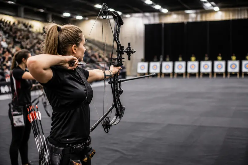 Compound archery event showcasing athletes aiming in a competitive indoor setting.